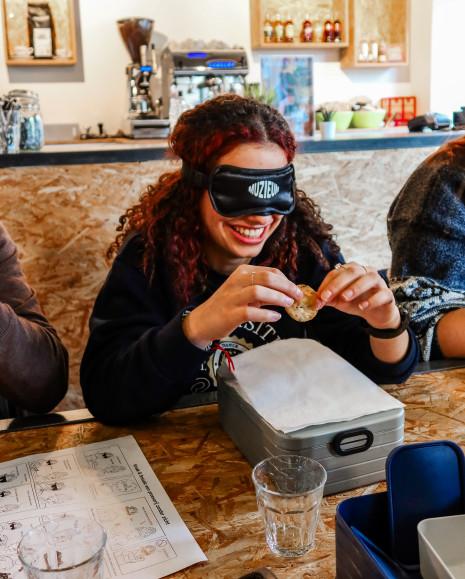 A visitor wearing a blindfold, holding a biscuit and feeling its texture.