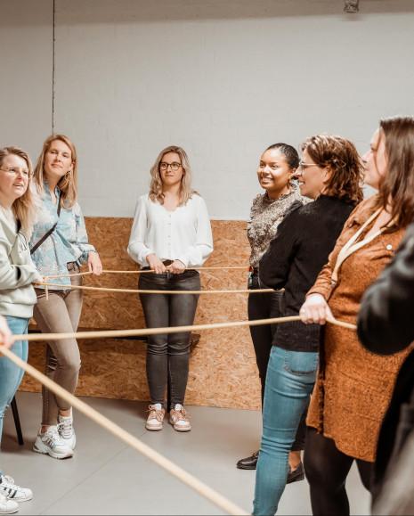 A group of visitors each holding a part of the same rope, communicating with one another to untangle it.