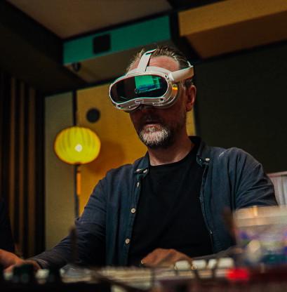 A visitor wearing an AR headset in their own studio, behind a mixing console, trying to operate the panel with low vision.