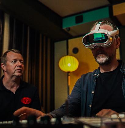 A visitor wearing an AR headset in their own studio behind a mixing console. They are trying to operate the panel with limited vision.