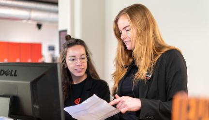 Fleur and Juni are conversing with each other at the reception desk of muZIEum.