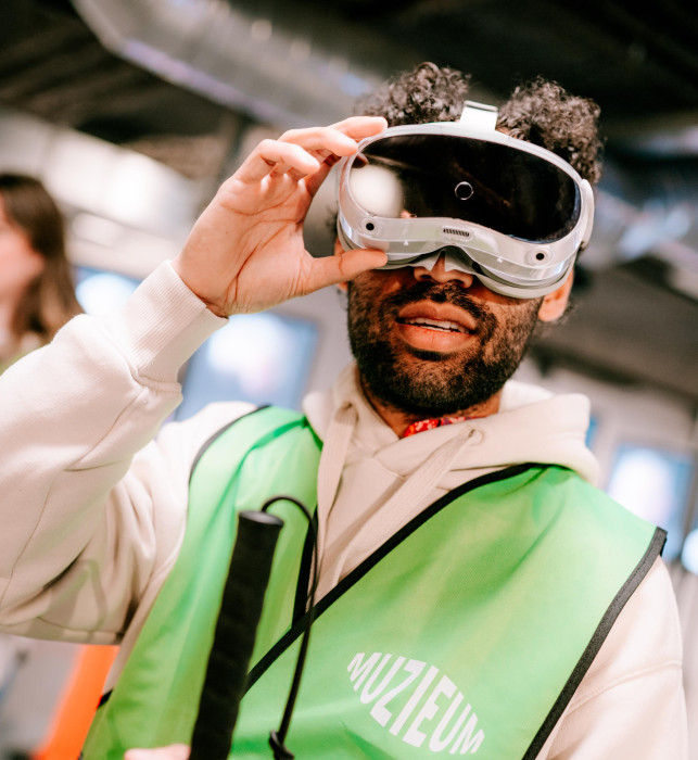 A visitor wearing an AR headset. With his right hand, he is holding onto the headset.