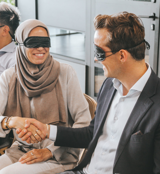 Two visitors are blindfolded and shaking hands.