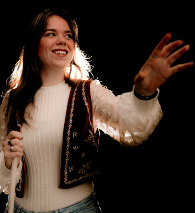 A visitor on the Tour in absolute dark, holding a white cane in one hand and extending the other hand out.