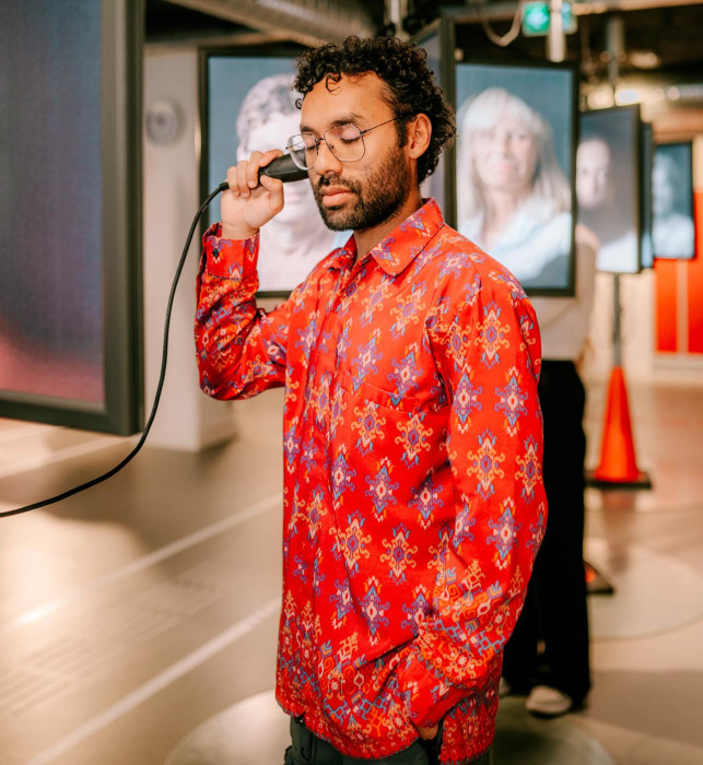 A visitor with their eyes closed and a hand in their pocket, listening to one of the stories of my vision through a listening horn at their ear.