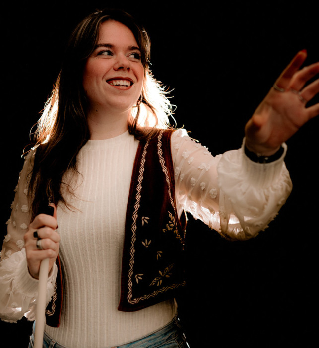 A visitor in the Tour in absolute darkness. She has her eyes open, extends her left hand forward, and holds a white cane in her right hand.